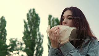 Woman is opening mouth and biting hamburger with appetite sitting outdoors in slow motion [upl. by Templeton5]